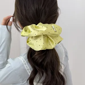 Vue arrière détaillée d'un chouchou en satin jaune à pois porté sur une queue de cheval
