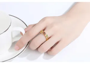 Gedetailleerde macro-opname van een gouden ring met dubbele rij gekleurde zirkoon op de hand.