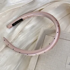 Vue détaillée d'un serre-tête rembourré en satin rose avec des pois noirs chic.