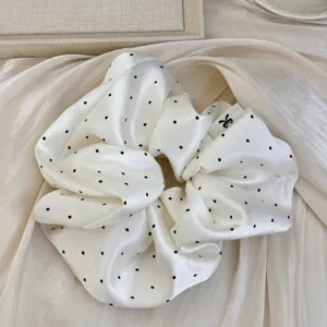 Détail d'un chouchou en satin blanc élégant avec des pois noirs et une texture douce