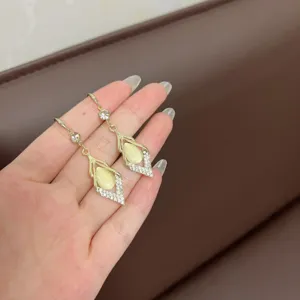 Detailansicht eleganter Goldohrringe mit Katzenaugenstein und schimmernden Strasssteinen