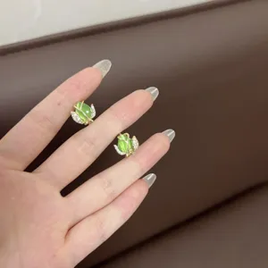 Detalle de elegantes pendientes de tulipán dorados con piedras de ojo de gato verdes.