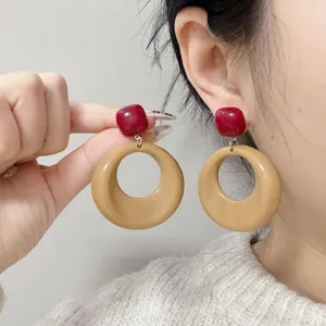 Close-up detail of retro geometric round drop earrings with red studs and khaki hoops