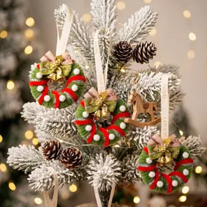 Festive mini Christmas wreath ornaments with gold bells hanging on a frosted tree