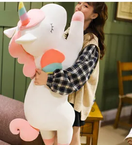 Soft large white unicorn plush toy with rainbow horn held by a girl in a cozy room