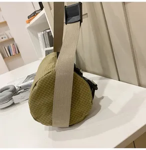 Detailed side view of khaki grid cylindrical crossbody bag with wide beige strap