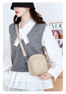 Dettaglio di una borsa a tracolla in nylon beige leggero indossata da una modella casual.