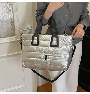 Silver metallic quilted puffer tote bag with black straps held by model in indoor setting