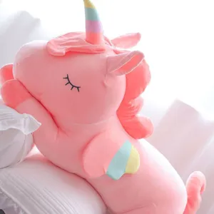 Soft large pink unicorn plush toy with rainbow wings and horn on white bedding.
