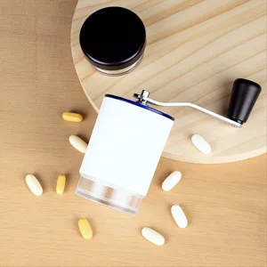 Top-down view of manual pill grinder on wooden tray with scattered vitamin tablets