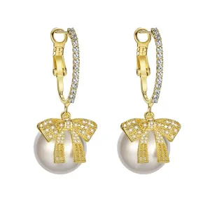 Elegant gold hoop earrings featuring a sparkling bow design with a white pearl drop.
