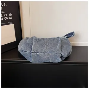 Close-up detail of a slouchy blue denim shoulder bag presented on a stylish black interior surface.