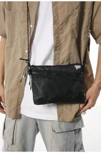 Detail view of a black utility crossbody bag with mesh pocket and reflective patch.
