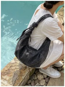 Fashionable acid wash denim hobo bag with knotted strap shown in a lifestyle poolside setting