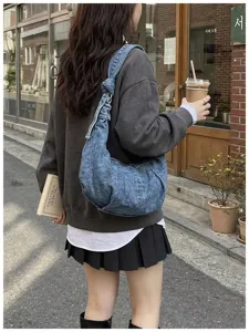 Detail view of a large denim hobo bag worn by a student in a casual street setting.