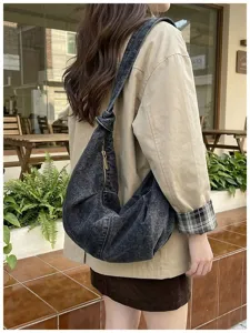 Close-up of a black washed denim hobo shoulder bag with a unique knot strap and gold zipper.