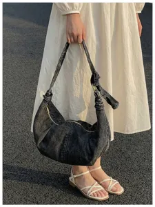 Detail view of a large capacity denim hobo bag held by a person in a white dress.