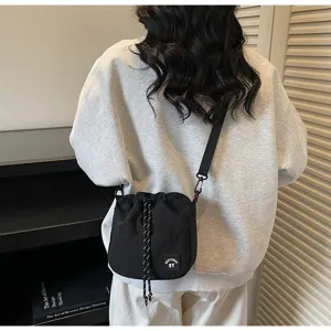 Zwarte nylon bucket bag met trekkoord gedragen door een model in een casual outfit.
