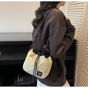 Detail van een crèmekleurige nylon bucketbag met trekkoord gedragen door een model