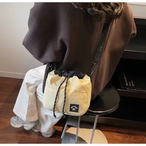 Casual crème nylon bucketbag met trekkoord gedragen als crossbodytas op een model