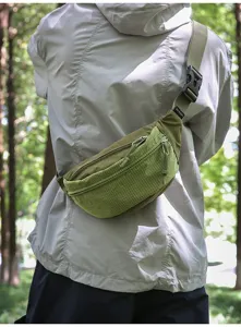 Back view of a green sporty nylon crossbody cycling bag worn outdoors in a park