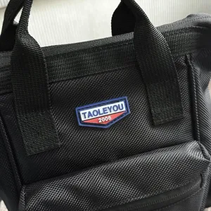 Gedetailleerde macro-weergave van de merklogo-patch op een zwarte canvas crossbodytas