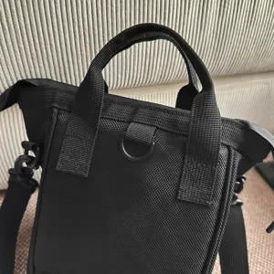 Detailopname van een zwarte nylon crossbodytas met stevige handvatten en een D-ring