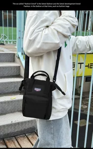 Kleine zwarte crossbodytas met rits aan de voorkant en handvat in streetstyle setting.