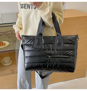 Detail view of a black quilted puffer tote bag carried by a model in a cozy cafe setting