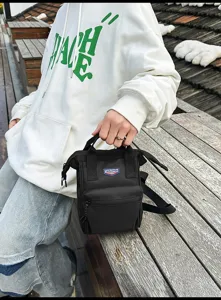 Close-up van een persoon die een zwarte casual crossbodytas met logodetail vasthoudt