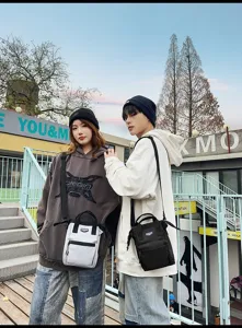 Lifestylefoto van twee modellen die trendy hoodies en kleine crossbodytassen buiten dragen