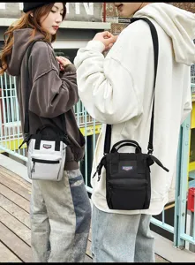 Outdoor straatstijl met twee mensen die compacte crossbodytassen in grijs en zwart dragen.
