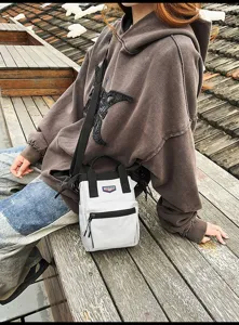 Kleine witte crossbody telefoontas gedragen door een model in een buitenomgeving.
