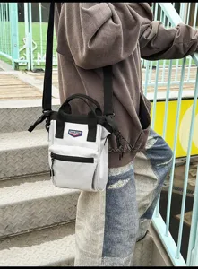 Detail van een grijze nylon crossbodytas op model met zwarte handvatten en riem
