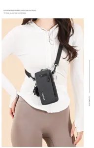 Slim black vertical crossbody phone bag shown on a model in a sporty white outfit.