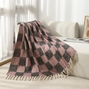 Soft pink and grey plaid blanket with tassels draped on a white sofa in sunlight