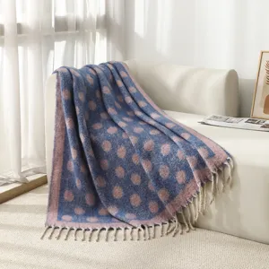 Détail d'une couverture jacquard à pois bleus et roses avec pompons doux sur un canapé