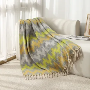 Soft yellow and grey jacquard throw blanket with decorative tassels draped over a sofa