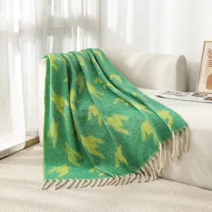 Manta acogedora de hilo bouclé de pata de gallo verde con borlas en un sofá blanco.