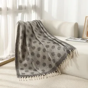 Couverture chaude à pois gris avec franges drapée sur un canapé blanc sous la lumière.