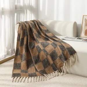 Detail view of a soft brown and grey checkered blanket with white tassel fringe on a sofa