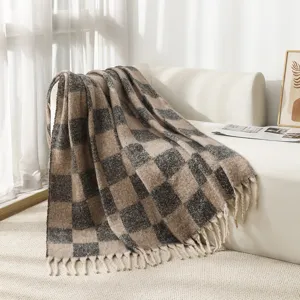 Cozy checkered mohair-like blanket with tassels draped on a white sofa in sunlight.
