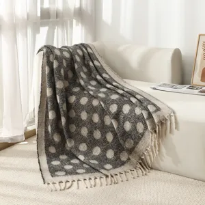 Couverture douce à pois en simili mohair avec pompons décoratifs sur un canapé blanc.