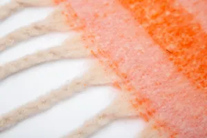 Detailaufnahme der weichen orangefarbenen Mohair-Boucle-Decke mit flauschigen Fransen