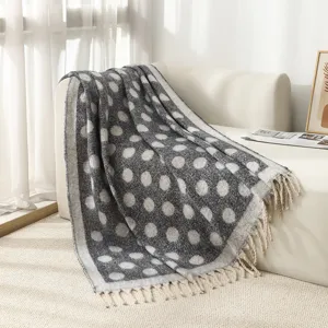 Détail d'une couverture en jacquard à pois avec des glands sur un canapé blanc