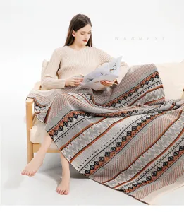 Model sitting on a sofa covered with a Bohemian knit throw blanket with ethnic patterns