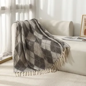 Jeté de canapé bouclé à losanges gris et blanc avec de longues franges sur un canapé blanc