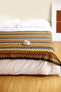 Vista detallada de la manta tejida de estilo bohemio con patrón de zigzag en cama