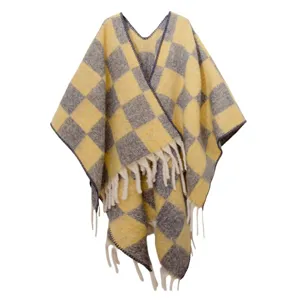 Gros plan sur le poncho en mohair à carreaux jaunes et gris avec garniture de glands.