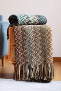 Detalle de manta bohemia de punto con patrones en zigzag y acentos de flecos tejidos.